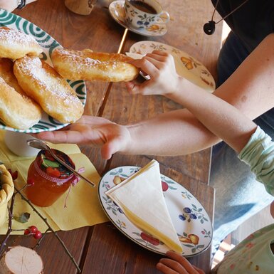 Kind nimmt sich einen Bauernkrapfen vom Teller | © Urlaub am Bauernhof Oberösterreich / Harald Puchegger