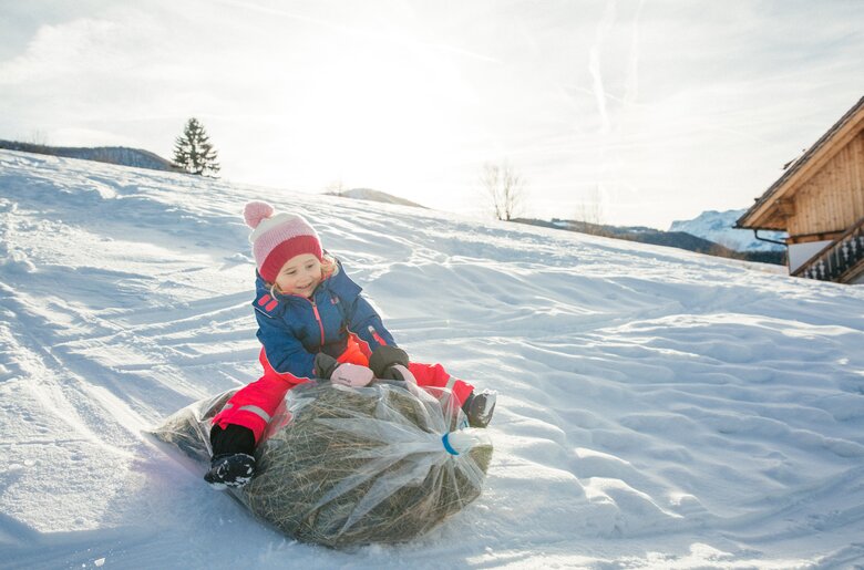Mädchen am Sackrutschen über den verschneiten Hang | © Urlaub am Bauernhof Oberösterreich / Pascal Baronit
