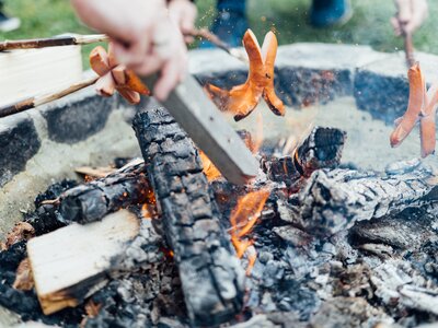 Mehrere Würstchen werden über Holzkohlegrill im Freien gegrillt, in Nahaufnahme