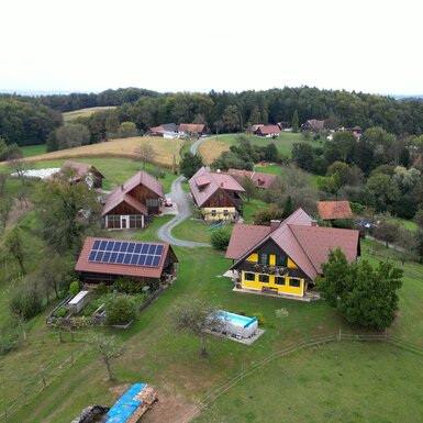 Ländliche Landschaft mit Holzhäusern, Gärten, Pool und Solarplatten, eingebettet in sanfte Hügel und Wälder. | © Urlaub am Bauernhof / Daniel Gollner