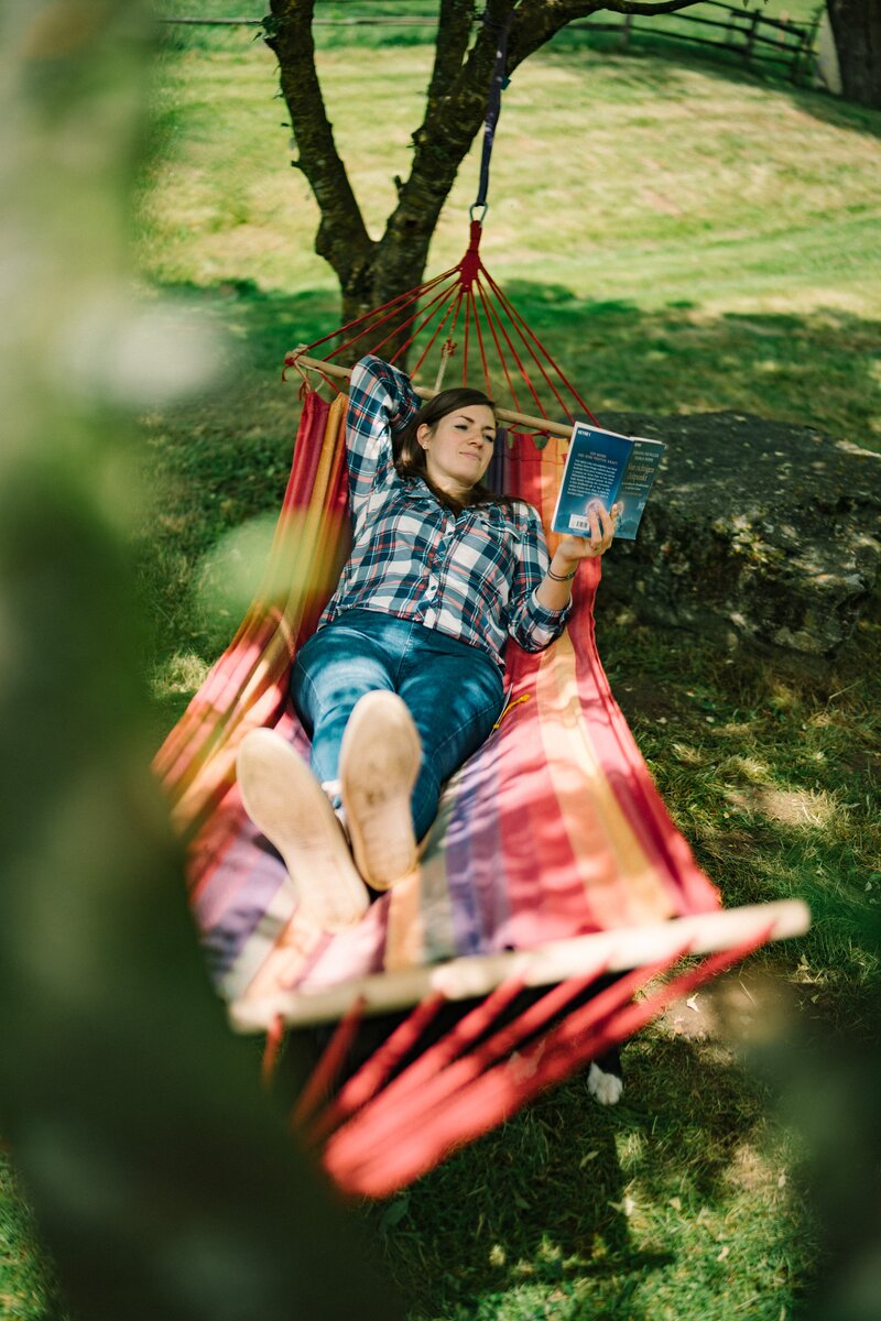 Eine Person, die in einer bunten Hängematte liegend ein Buch liest, umgeben von grüner, üppiger Natur. | © Urlaub am Bauernhof / Daniel Gollner 