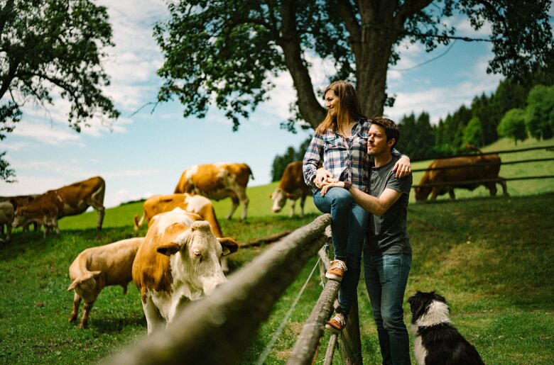 Ein junges Paar genießt die ländliche Umgebung mit Weidetieren auf der grünen Wiese, begleitet von einem Hund. | © Urlaub am Bauernhof / Daniel Gollner 