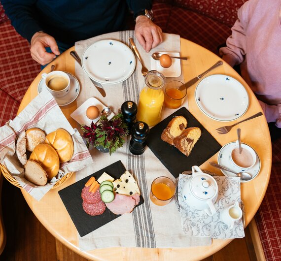 Ein Frühstückstisch mit verschiedenen Broten, Käse, Wurst, Eiern, Säften und Kaffee, serviert in einer gemütlichen Umgebung.