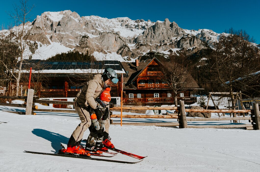 Zwei Skifahrer üben auf einer verschneiten Piste mit Bergen im Hintergrund.