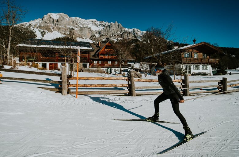 Person beim Skitouren in einer verschneiten Winterlandschaft, mit Bergen im Hintergrund und traditionellen Holzhäusern.