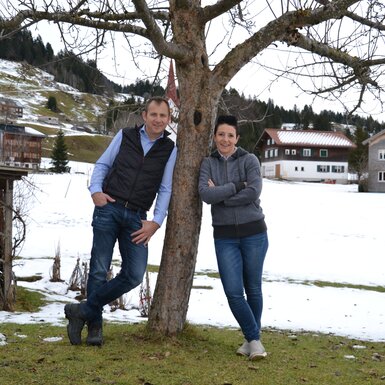 Bauer und Baeuerin lehnen am Baum vor verschneiter Wiese | © Urlaub am Bauernhof Österreich / Dorner