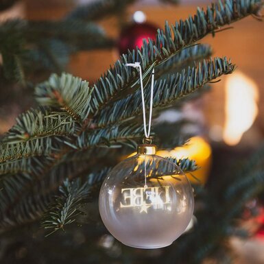 Die Nahaufnahme zeigt eine weihnachtliche Christbaumkugel mit der Aufschrift "LIEBE" an den Zweigen eines evergrünen Nadelbaums, umgeben von Schnee und einer warmen goldenen Beleuchtung. | © Urlaub am Bauernhof / Pascal Baronit