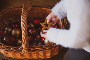 Weihnachtsdeko in Flechtkorb | © Urlaub am Bauernhof / Pascal Baronit Eine Hand in einem weißen Pelzmantel hält einen goldenen Stern über einem Korb voller bunter Weihnachtskugeln. | © Urlaub am Bauernhof / Pascal Baronit