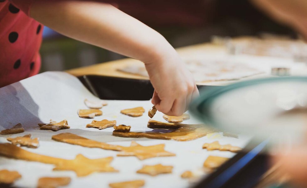 Eine Person bäckt Plätzchen mit Ausstechformen in Sternform auf einer Arbeitsplatte, umgeben von fertigen Keksen. | © Urlaub am Bauernhof / Pascal Baronit