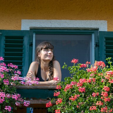 Frau auf blumengeschmücktem Balkon | © Urlaub am Bauernhof im SalzburgerLand / www.travelpins.at