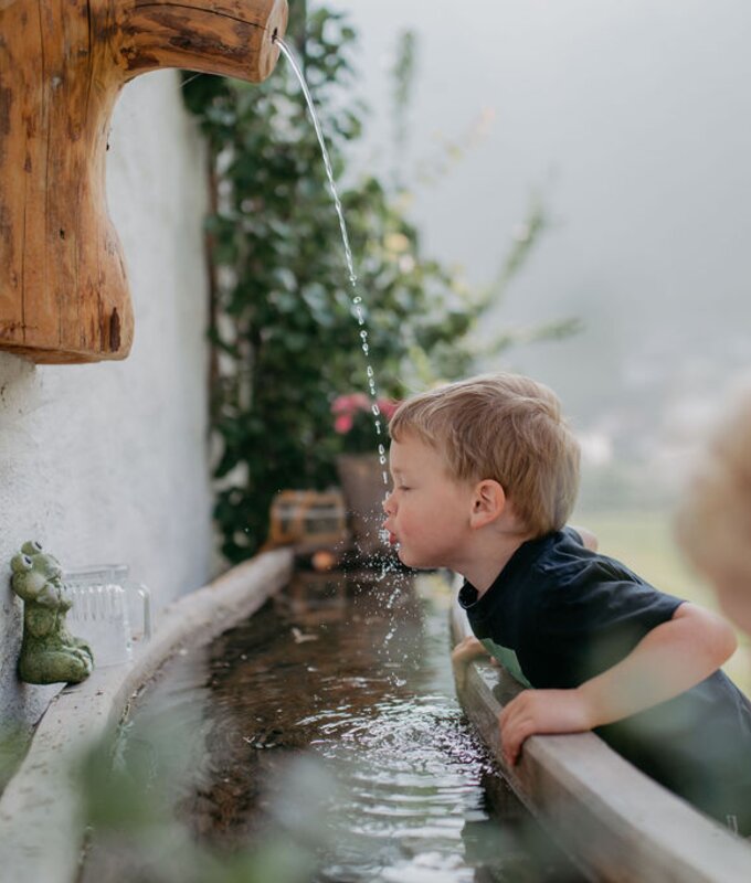 Bub trinkt Wasser aus Wasserstrahl | © Urlaub am Bauernhof/ Nadja Jabli