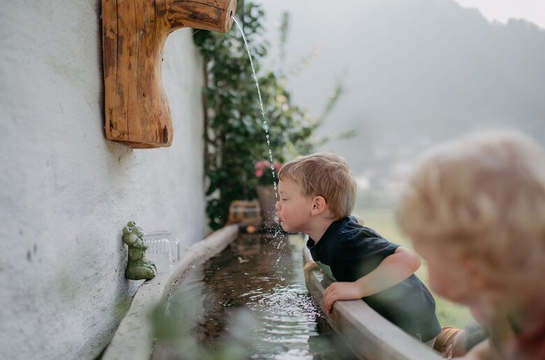 Bub trinkt Wasser aus Wasserstrahl | © Urlaub am Bauernhof/ Nadja Jabli