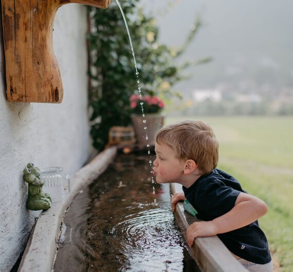 Bub trinkt Wasser aus Wasserstrahl | © Urlaub am Bauernhof/ Nadja Jabli