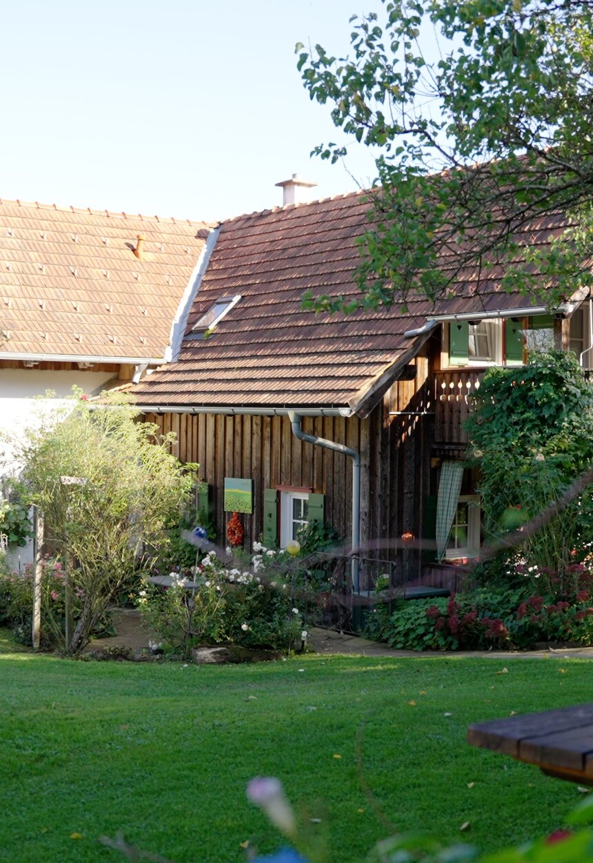 Ein altes Nebengebäude am Bauernhof, das als Ferienhaus liebevoll renoviert wurde, Aufgang zum Eingang ist eine Holzstiege, davor befindet sich eine gepflegte Wiese mit Sitzmöbeln aus Holz | © Urlaub am Bauernhof Steiermark / Daniel Gollner