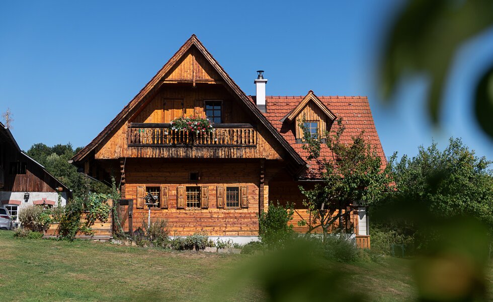 Ein großes Bauernhaus aus Holz mit Wiese und Sträuchern im Vordergrund | © Urlaub am Bauernhof / Carletto Ferrari-Brunnenfeld 