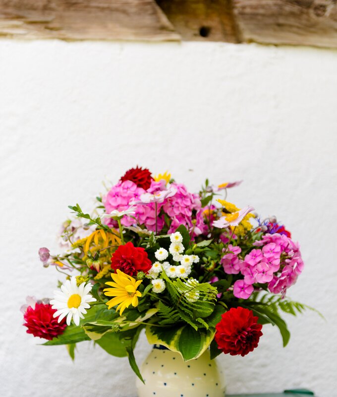 Eine weiße, bauchige Blumenvase mit grünen Punkten steht auf einem grün lackierten Tisch vor weißen Hintergrund, darin ein üppiger Strauß mit roten, gelben, weißen, rosa Sommerblumen aus dem Garten | © Urlaub am Bauernhof Steiermark / Wolfgang Spekner
