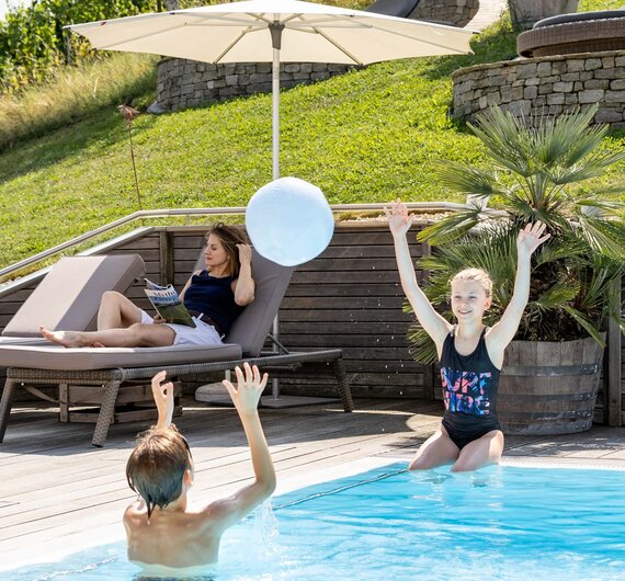 Ein Bub und ein Mädchen spielen im Pool Wasserpool, die Mutter liegt im Liegestuhl und liest | © Urlaub am Bauernhof / Elisabeth Fröhlich photography