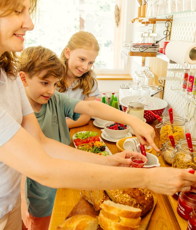Eine Mutter steht mit ihrem Sohn und ihrer Tochter am Frühstücksbuffet und gibt Marmelade in ein Schälchen | © Urlaub am Bauernhof Steiermark / Wolfgang Spekner