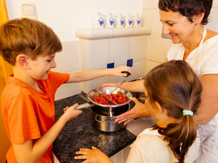 Ein Bub und ein Mädchen passieren mit einer flotten Lotte die Ribisel für die Marmelade, die Bäuerin hält den Topf | © UaB Steiermark | Wolfgang Spekner