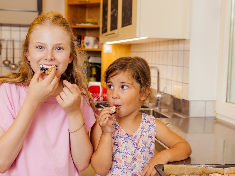 Zwei Mädchen essen mit Genuss einen frischgebackenen Blechkuchen mit Obst, der mit Staubzucker bestreut ist | © UaB Steiermark | Wolfgang Spekner