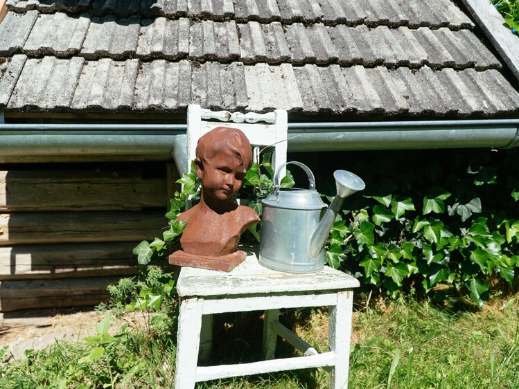Tonkopf eines Kindes und alte gusseiserne Gießkanne als Dekoration im Garten, Biobauernhof Leitenmüller, Steiermark | © Urlaub am Bauernhof Steiermark / Daniel Gollner