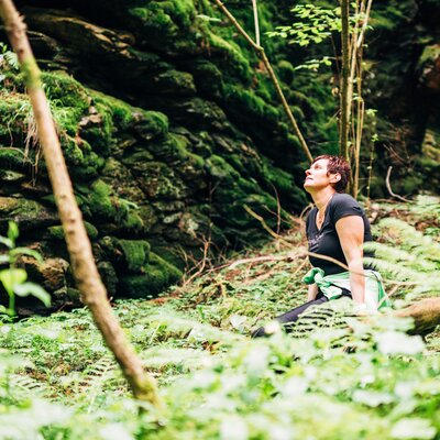 Frau beim Waldbaden auf einer Lichtung sitzend | © Urlaub am Bauernhof Steiermark / Daniel Gollner