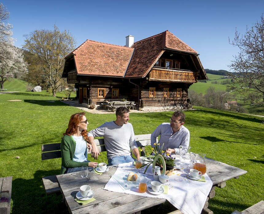 Der Bauer sitzt mit seinen Gästen beim österlich gedeckten Kaffeetisch im Freien, Steiermark | © Urlaub am Bauernhof Steiermark / Tom Lamm