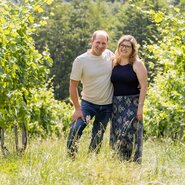 Ein Mann und eine Frau stehen im Weingarten zwischen den Rebreihen im Grünen | © Weingut & Buschenschank Pölzl / Fam. Pölzl