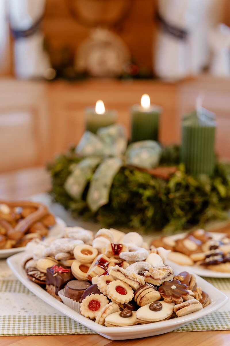 Ein volles Teller mit verschiedenen Weihnachtskeksen steht auf dem Tisch. Davor sieht man den Adventkranz, auf dem zwei Kerzen leuchten. | © UaB Steiermark / Wolfgang Spekner