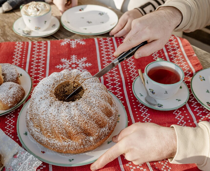 Eine Kaffeepause im Freien vor dem Bauernhaus. Ein Mann schneidet einen Gugelhupf an. Drum herum stehen Kaffeetassen und Teller.  | © UaB Steiermark / Wolfgang Spekner