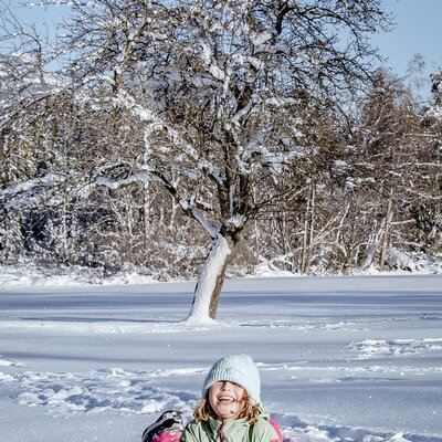 Ein Mädchen ist im in der Sonne glitzernden Tiefschnee eingesunken und zeigt lachend den Daumen hoch | © Urlaub am Bauernhof Steiermark / Wolfgang Spekner