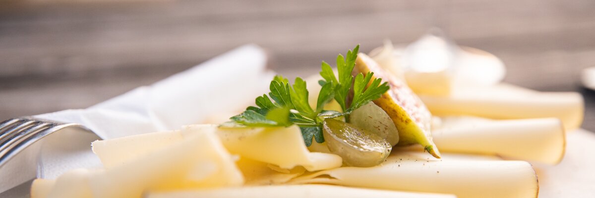 Appetitlich aufgelegte Käschescheiben auf einem Holzbrett, garniert mit Weintraube, Petersilie und frischer Feige | © Urlaub am Bauernhof / punkt & komma