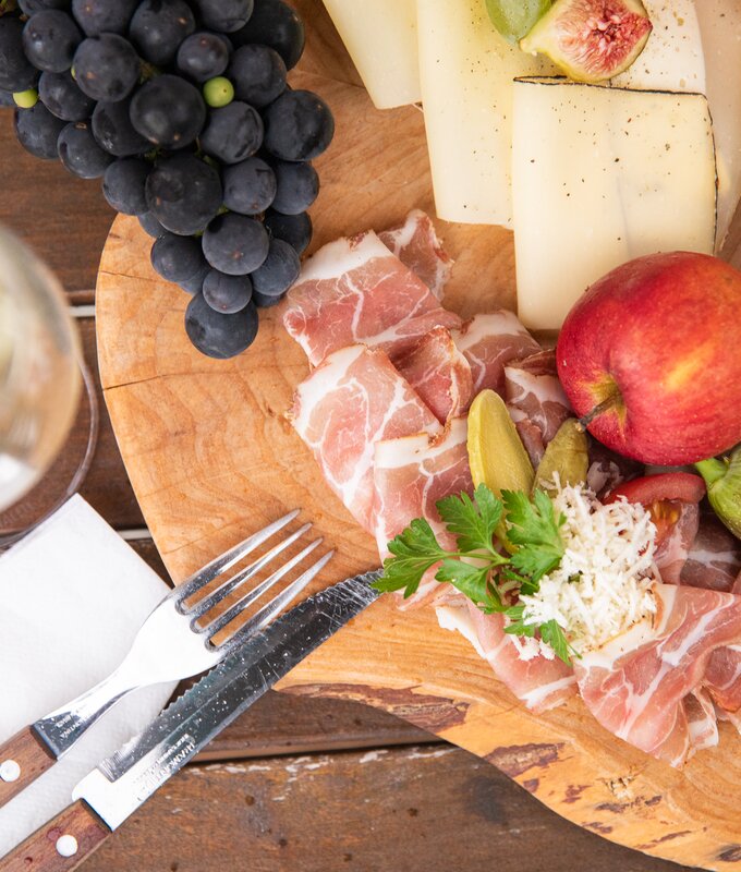 Eine herzhafte steirische Brettljause am Holzbrett serviert, mit Würsteln, Speck, Rohschinken, Käse, Weintrauben, Äpfeln, frischen Feigen und Käferbohnensalat | © Urlaub am Bauernhof / punkt & komma