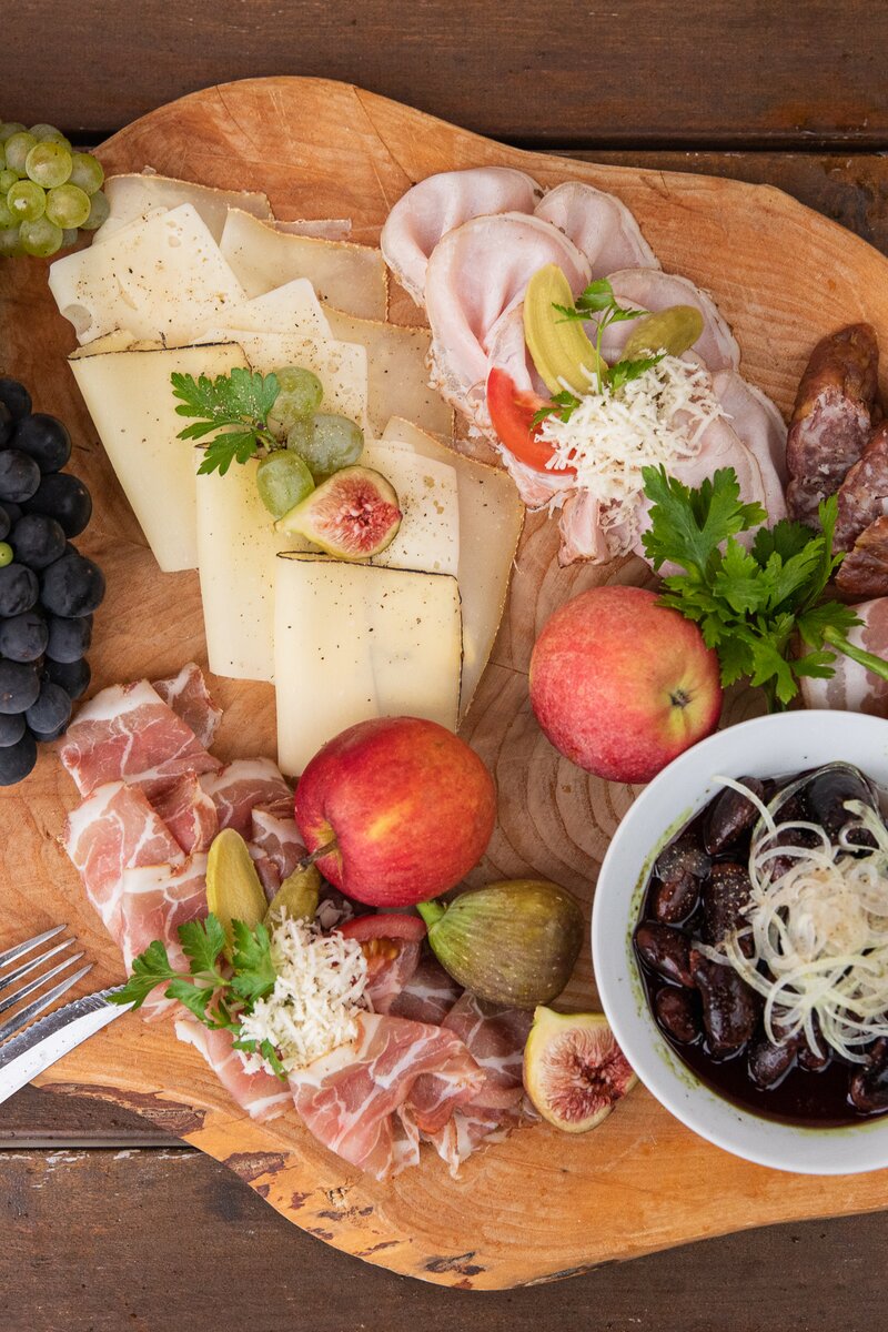 Eine herzhafte steirische Brettljause am Holzbrett serviert, mit Würsteln, Speck, Rohschinken, Käse, Weintrauben, Äpfeln, frischen Feigen und Käferbohnensalat | © Urlaub am Bauernhof / punkt & komma