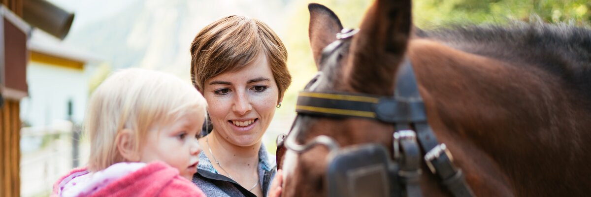 Mutter mit Tochter am Arm beim Pferd | © Urlaub am Bauernhof Vorarlberg / Daniel Gollner