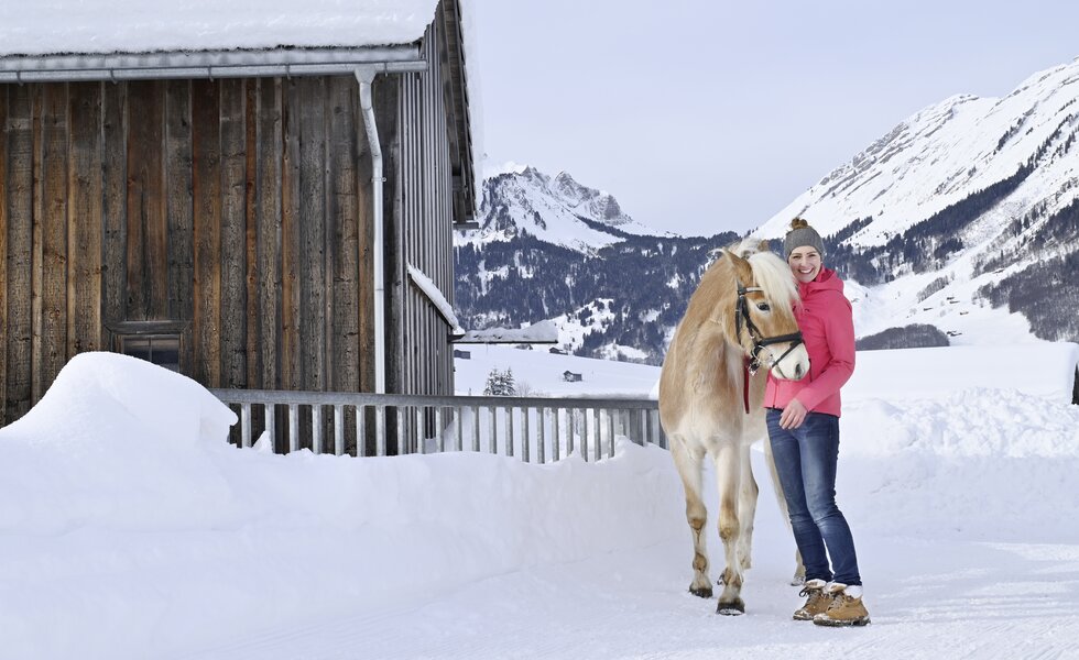 Eine Frau steht in der Winterlandschaft mit einem Pferd | © Urlaub am Bauernhof / Andreas Künk