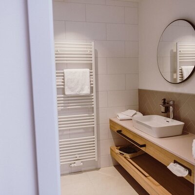 Das Badezimmer im Hof mit großem Waschtisch, rundem Spiegel und Handtuchheizkörper.