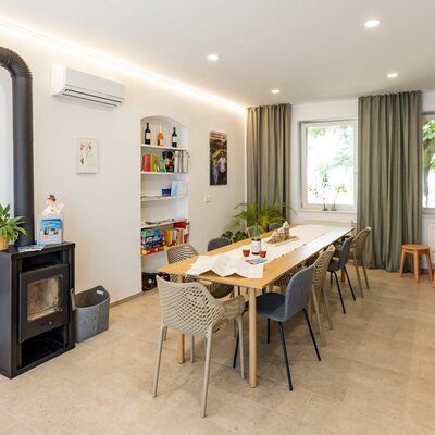 Der gemütliche Eingangsbereich und Aufenthaltsraum des Hauses mit Esstisch, Kaminofen, Klimaanlage und einer Bücherecke mit regionalen Informationen.