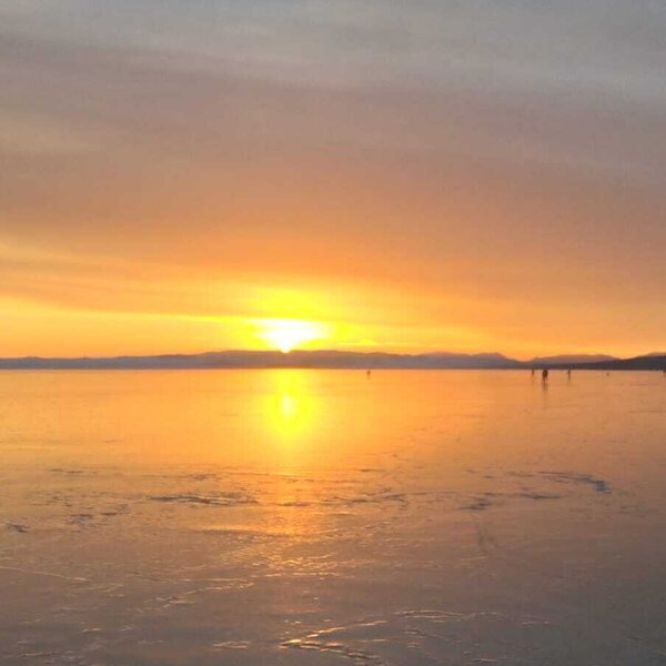Ein stimmungsvoller Sonnenuntergang über dem weiten, vereisten See in der Nähe des Bauernhofs.
