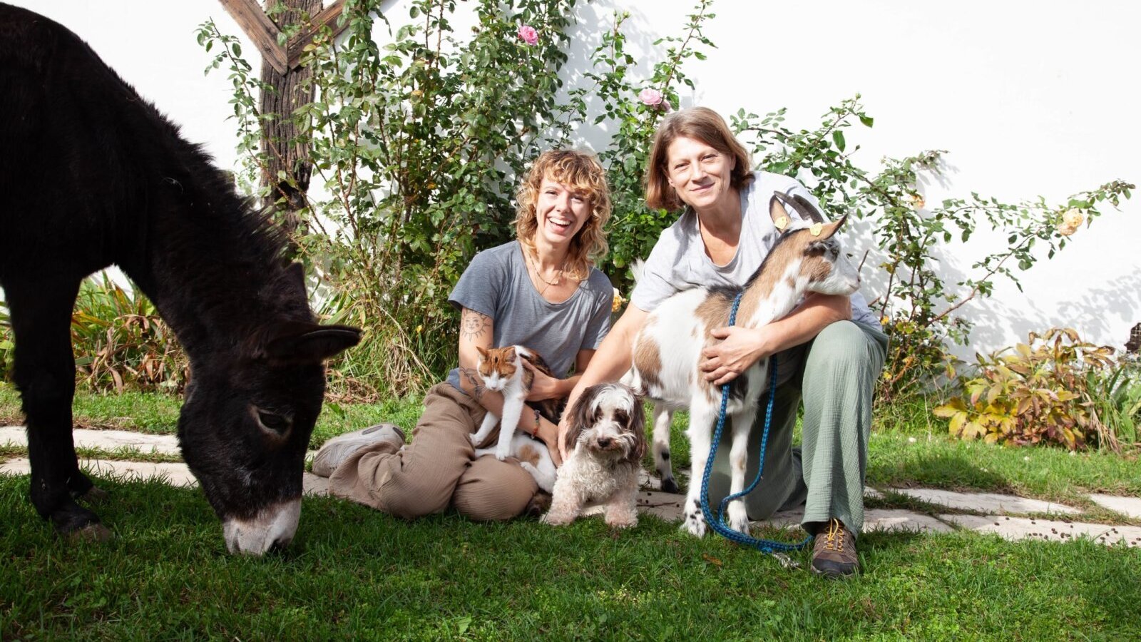 Die herzlichen Gastgeber Maria und Larissa inmitten ihrer zutraulichen Tiere auf einer grünen Wiese.