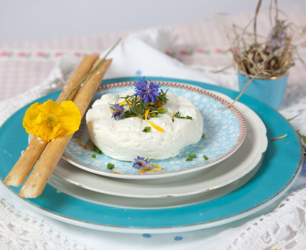 Frischer, liebevoll mit bunten Blüten garnierter Bio Ziegenkäse, der im Bed and Breakfast mit knusprigen Grissini serviert wird.