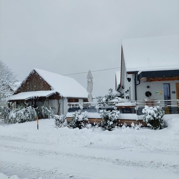 Der Bauernhof im Winter, mit schneebedeckten Gebäuden und einer Terrasse.