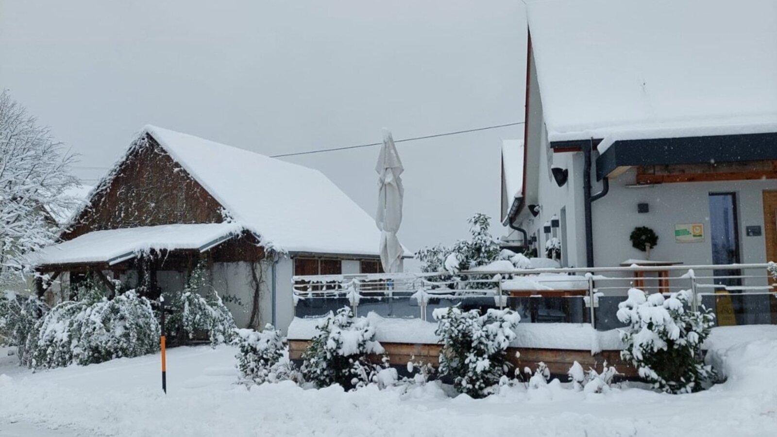 Der Bauernhof im Winter, mit schneebedeckten Gebäuden und einer Terrasse.