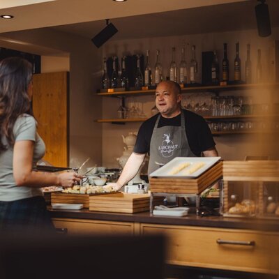 Der Gastgeber am Frühstücksbuffet des Bauernhofs, der mit einem Gast spricht.
