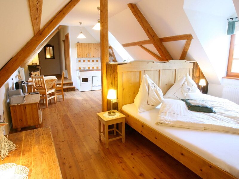 Das Schlafzimmer im Dachgeschoss des Bauernhofs verfügt über ein Doppelbett aus Holz, Holzbalken, einen Holzboden sowie eine integrierte Küchenzeile und einen Essbereich.