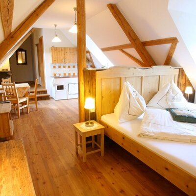 Das Schlafzimmer im Dachgeschoss des Bauernhofs verfügt über ein Doppelbett aus Holz, Holzbalken, einen Holzboden sowie eine integrierte Küchenzeile und einen Essbereich.