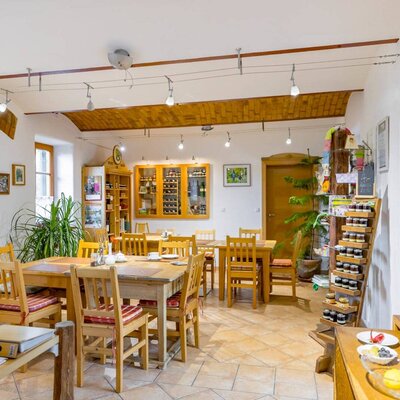 Der Essbereich des Bauernhofs mit Holztischen, Stühlen, gefliestem Boden und einem Regal mit lokalen Produkten.