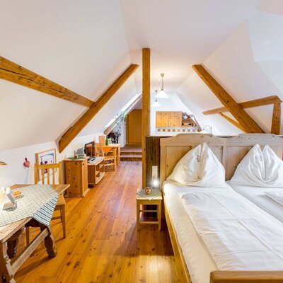 Dachgeschoss-Schlafzimmer Laubwald mit Doppelbett, Holzboden, sichtbaren Holzbalken und einem separaten Essbereich.