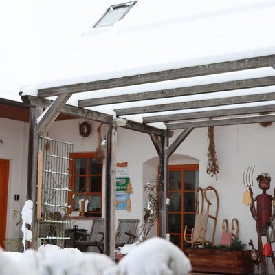 Der verschneite Außenbereich des Bauernhofs mit einer Holzpergola und rustikalen Dekorationen im Winter.