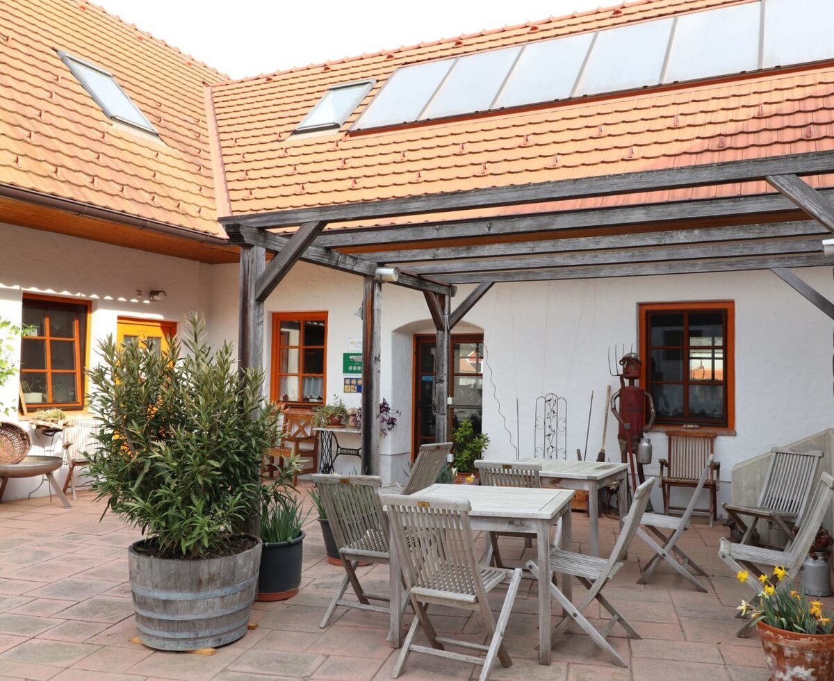 Der gepflasterte Innenhof des Bauernhofs mit Holztischen und -stühlen unter einer Pergola.
